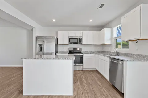 a kitchen with stainless steel appliances granite countertop a stove top oven a sink a refrigerator and white cabinets with wooden floor