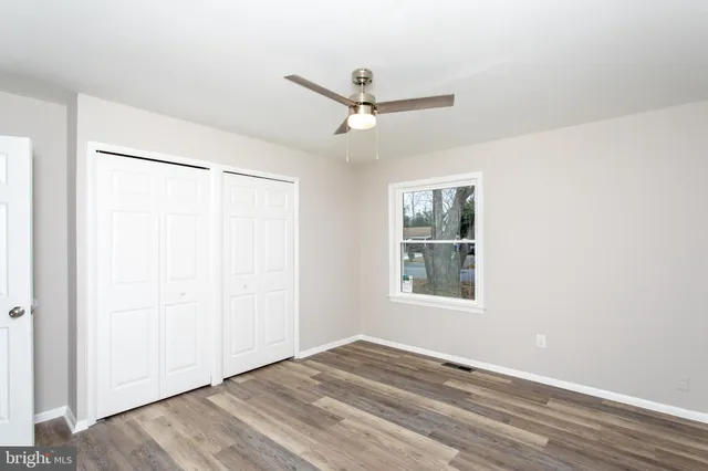 an empty room with wooden floor fan and windows