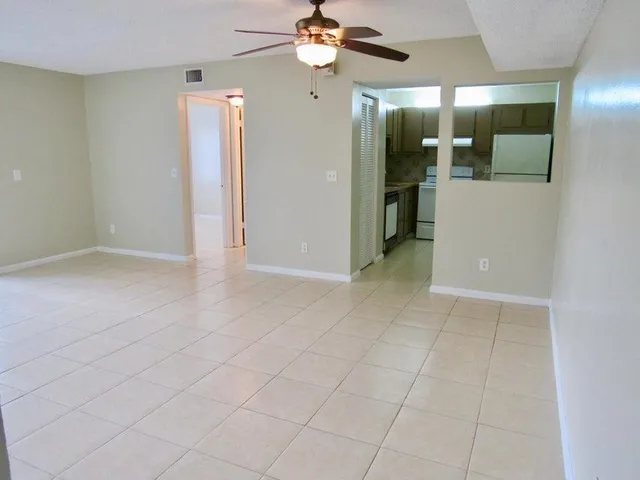 an empty room with kitchen and a chandelier fan