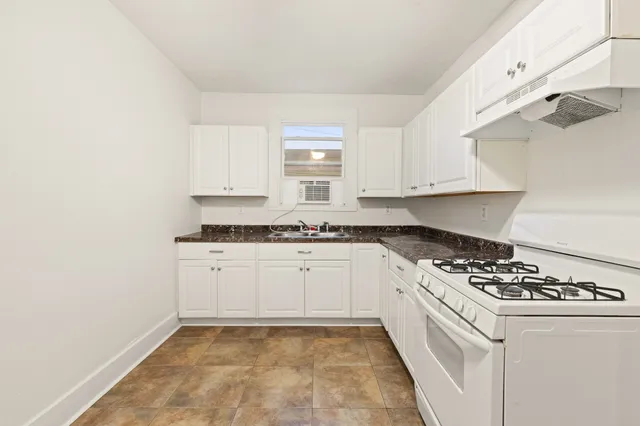 a kitchen with granite countertop a stove a sink and white cabinets