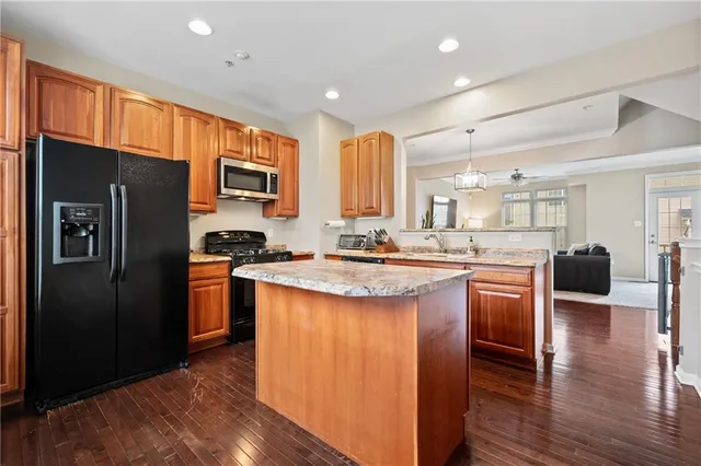 a kitchen with stainless steel appliances granite countertop a refrigerator a sink dishwasher a stove and a dining table with wooden floor