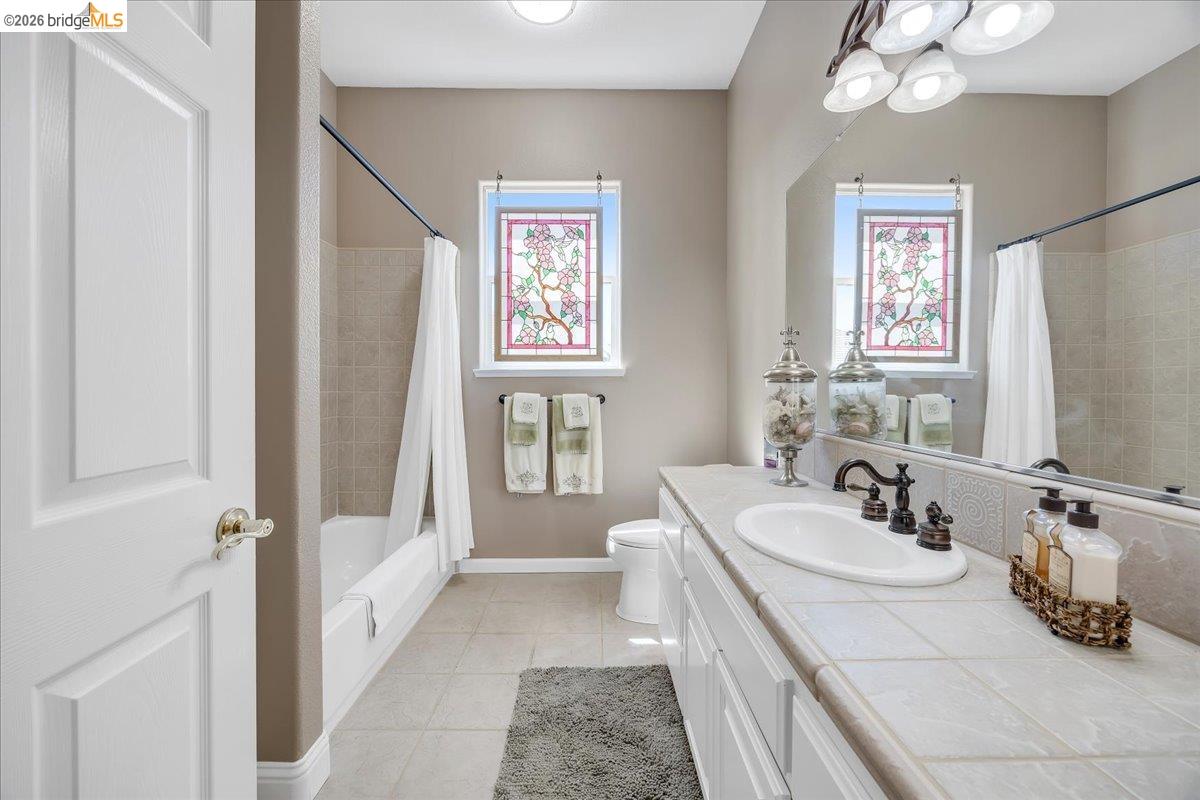 158 Rock Ridge Lane Copperopolis, CA 95228 - Photo 43 of 72 Bathroom featuring a tiled vanity with an undermount sink, a large mirror, and two windows with decorative stained glass panels