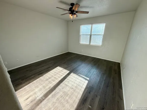 an empty room with wooden floor ceiling fan and windows