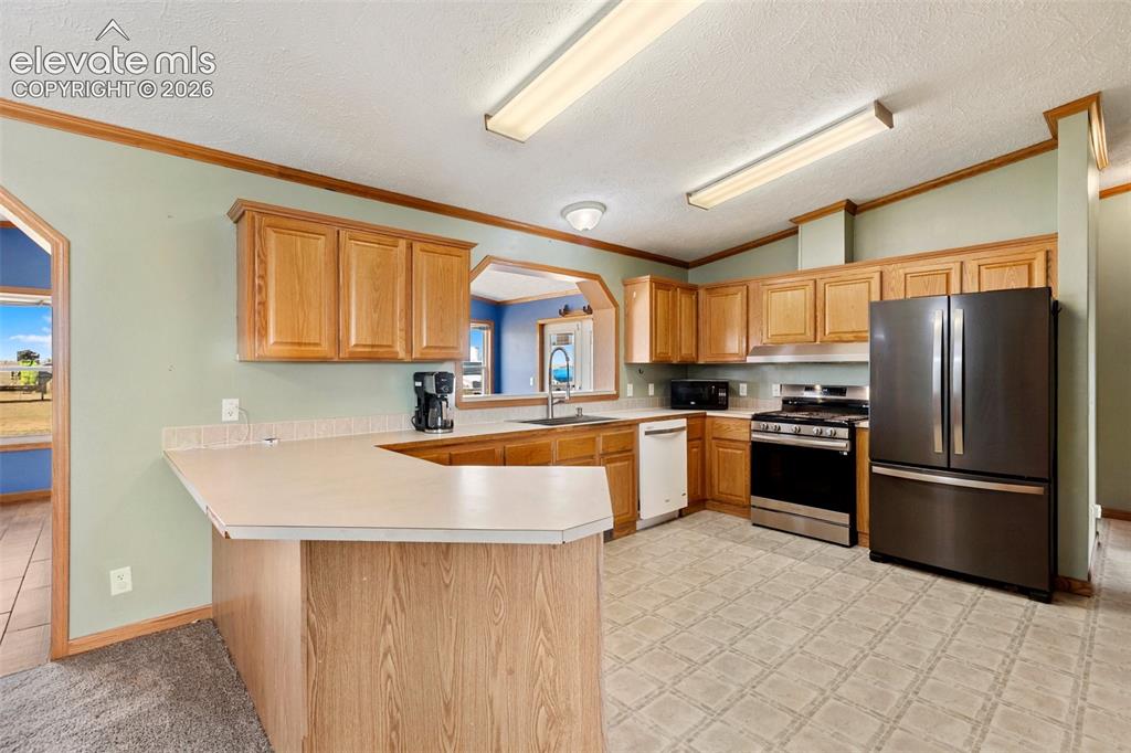 1350 South Calhan Highway Yoder, CO 80864 - Photo 21 of 45 Kitchen featuring wood-finish cabinetry, a breakfast bar, and a stainless steel appliance suite including a refrigerator, range, and dishwasher
