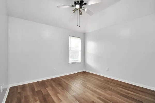 an empty room with wooden floor chandelier fan and windows