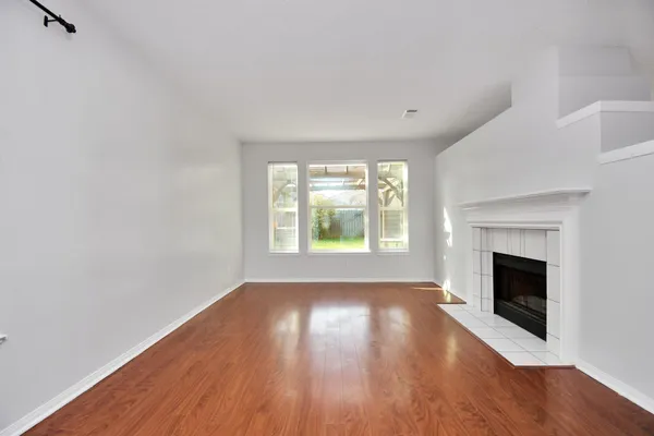 an empty room with wooden floor fireplace and windows