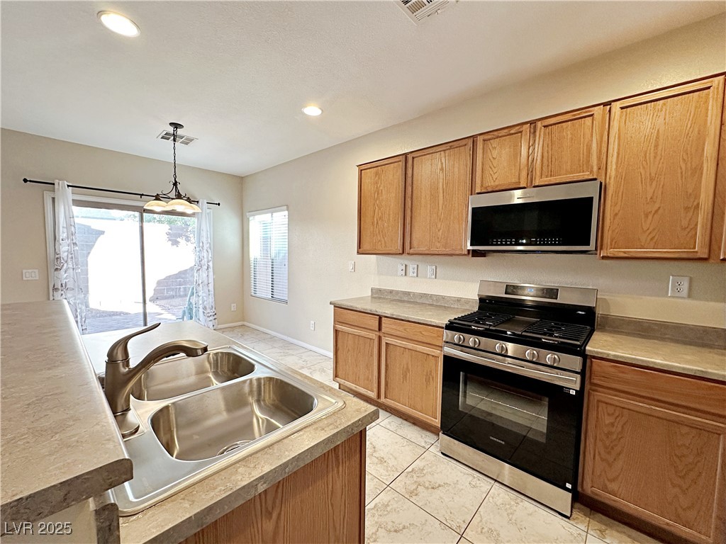 9620 Sharp Horn Court Las Vegas, NV 89149 - Photo 13 of 40 Kitchen with stainless steel appliances, pendant lighting, light countertops, brown cabinets, and light tile patterned flooring