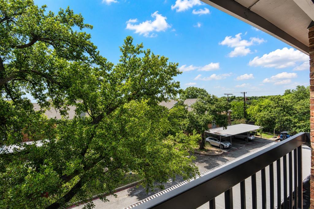 18333 Roehampton Drive, Unit 1036 Dallas, TX 75252 - Photo 4 of 12 Balcony with black metal railings overlooking a paved parking area with covered parking structures and surrounding mature trees