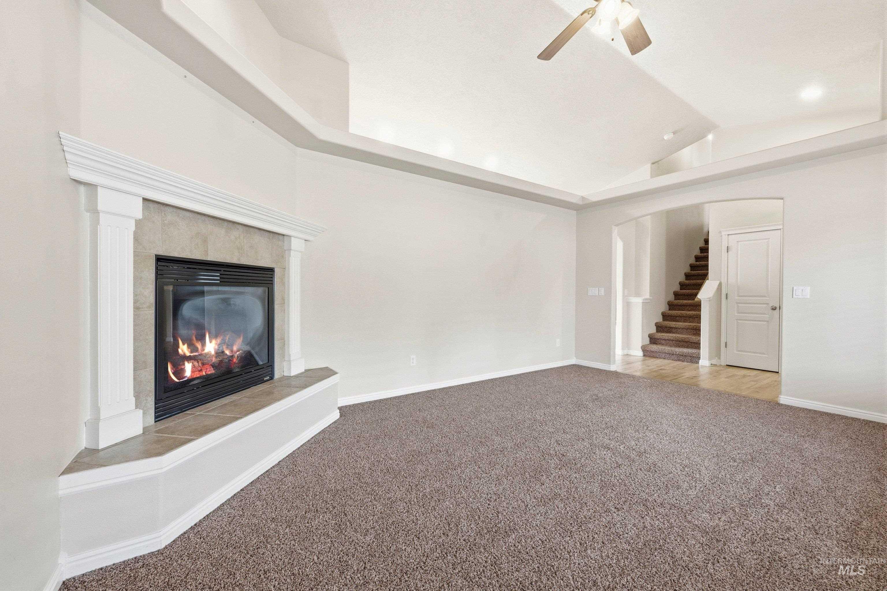 3787 North Alexis Way Meridian, ID 83646 - Photo 11 of 50 Unfurnished living room featuring a ceiling fan, arched walkways, carpet, a tiled fireplace, and lofted ceiling