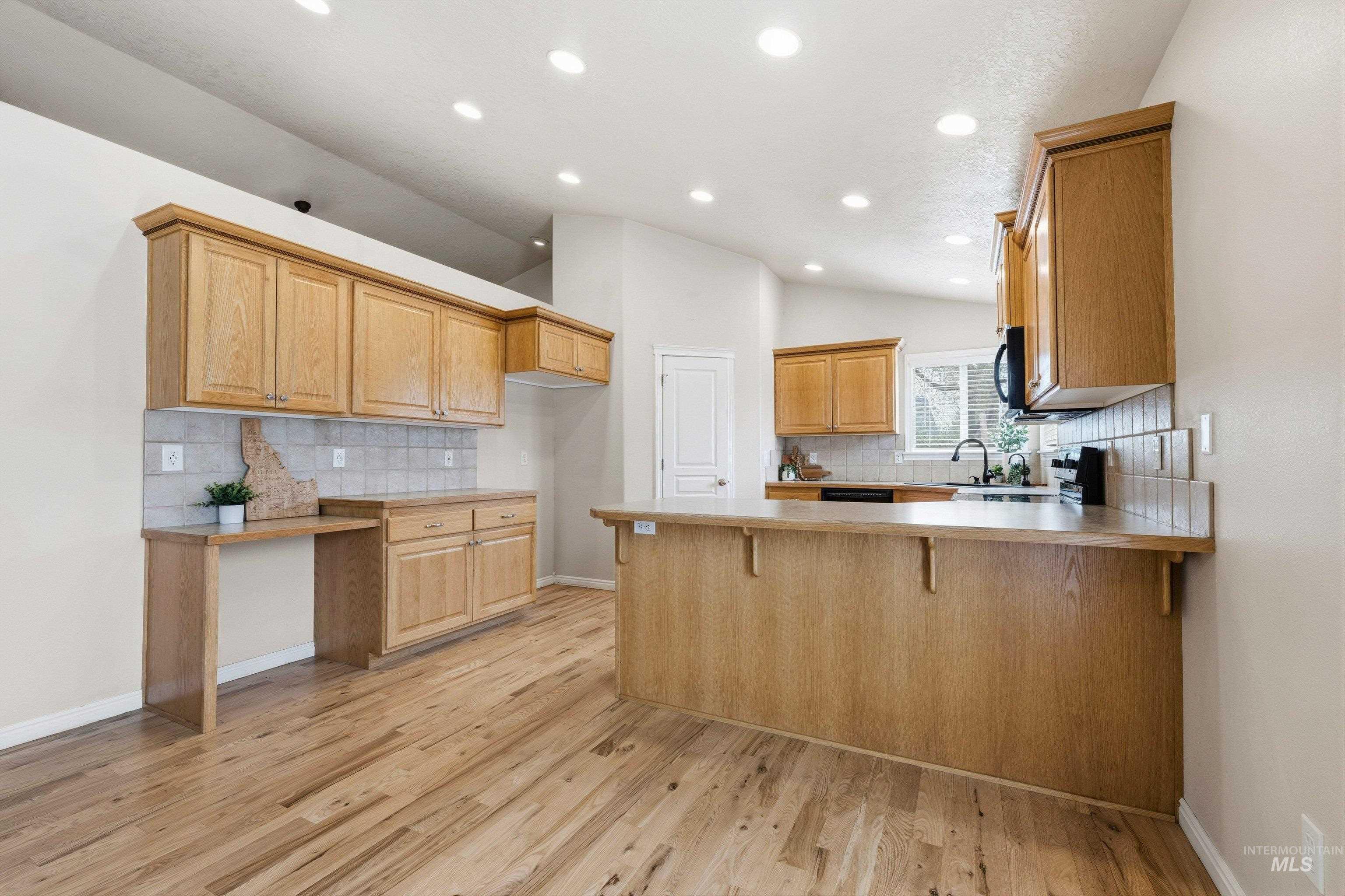 3787 North Alexis Way Meridian, ID 83646 - Photo 15 of 50 Kitchen featuring a peninsula, decorative backsplash, a kitchen bar, light wood-type flooring, and vaulted ceiling