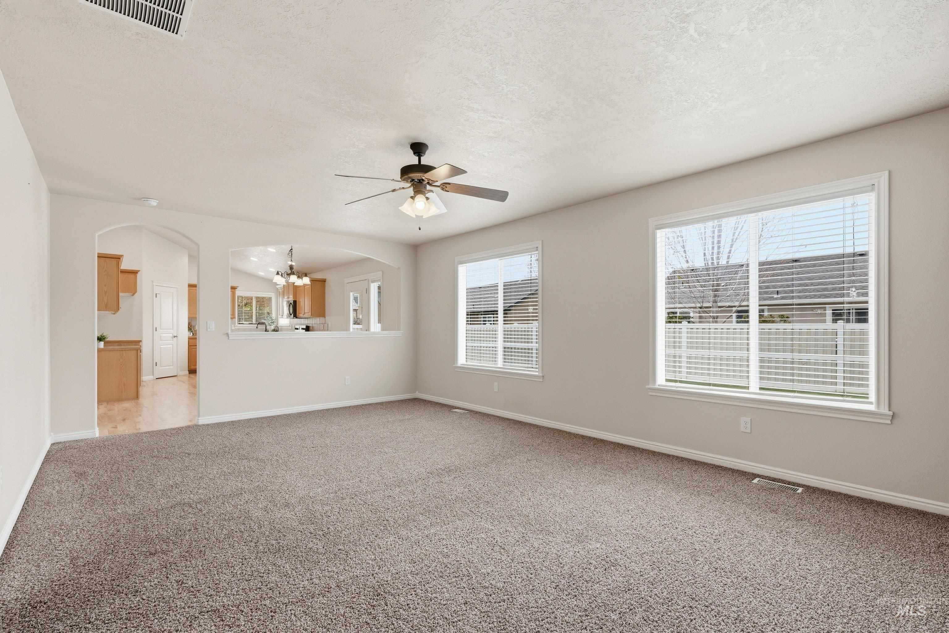 3787 North Alexis Way Meridian, ID 83646 - Photo 24 of 50 Unfurnished living room featuring carpet floors, arched walkways, ceiling fan, and a textured ceiling