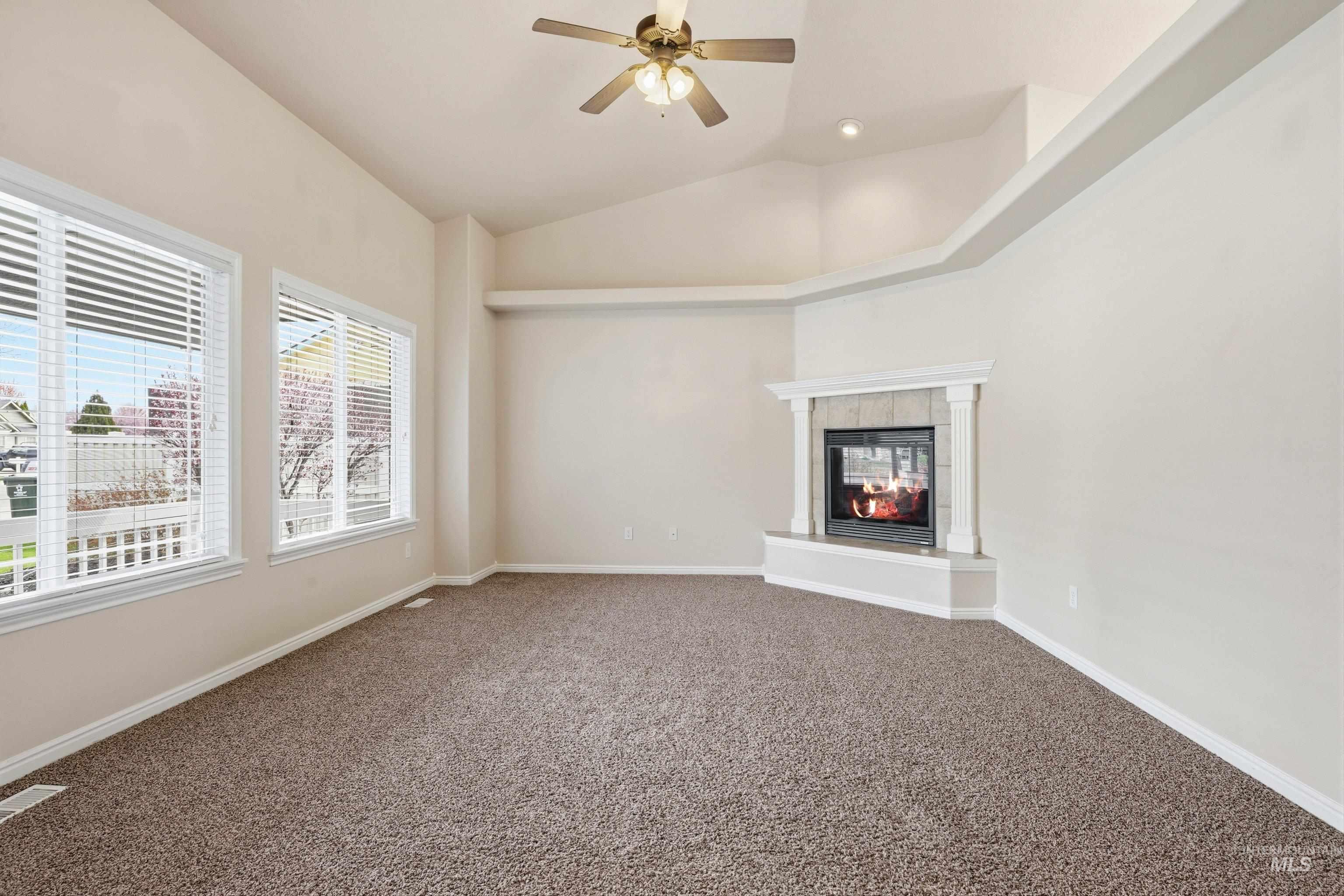 3787 North Alexis Way Meridian, ID 83646 - Photo 8 of 50 Unfurnished living room featuring dark colored carpet, a tiled fireplace, a ceiling fan, and lofted ceiling