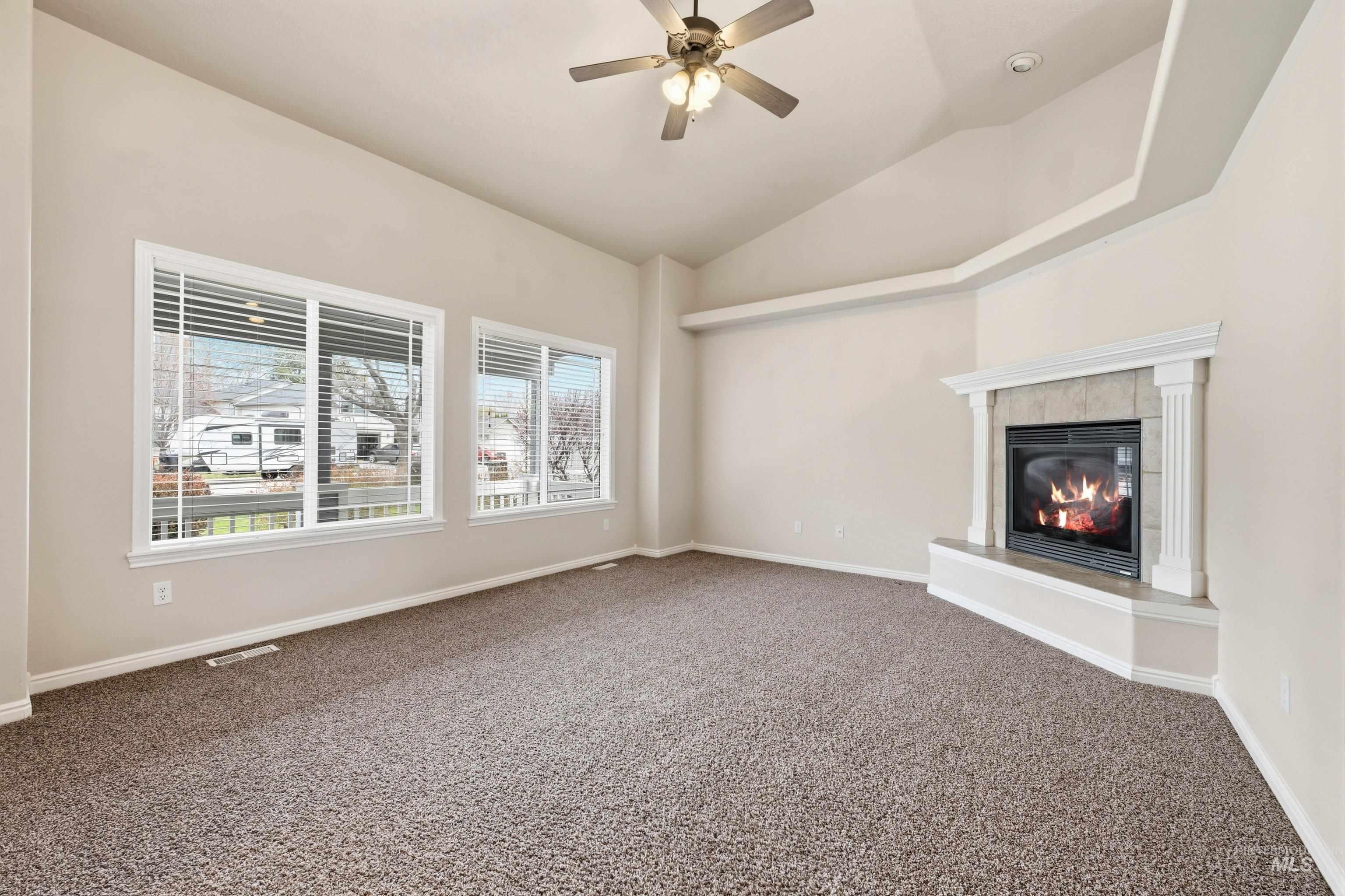 3787 North Alexis Way Meridian, ID 83646 - Photo 9 of 50 Unfurnished living room with dark carpet, a tiled fireplace, a ceiling fan, and lofted ceiling