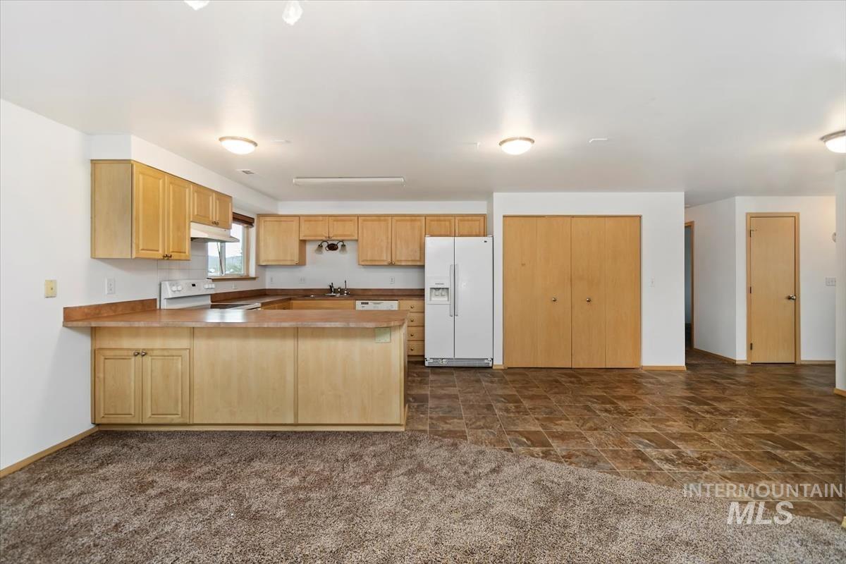1051 Haas Road Weiser, ID 83672 - Photo 11 of 44 Kitchen featuring white appliances, a peninsula, stone finish floors, light wood finish cabinets, and light countertops
