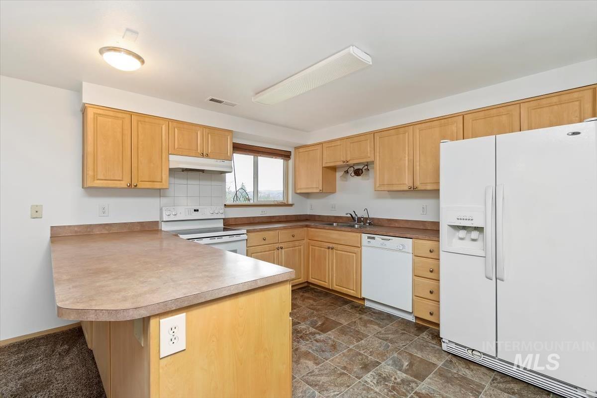1051 Haas Road Weiser, ID 83672 - Photo 12 of 44 Kitchen featuring white appliances, stone finish floors, light wood finish cabinets, light countertops, and decorative backsplash