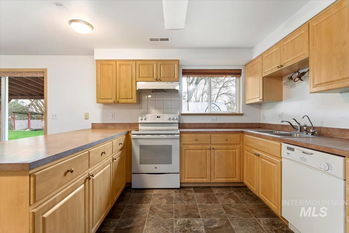 1051 Haas Road Weiser, ID 83672 - Photo 13 of 44 Kitchen with white appliances, a peninsula, stone finish flooring, and light wood finish cabinetry