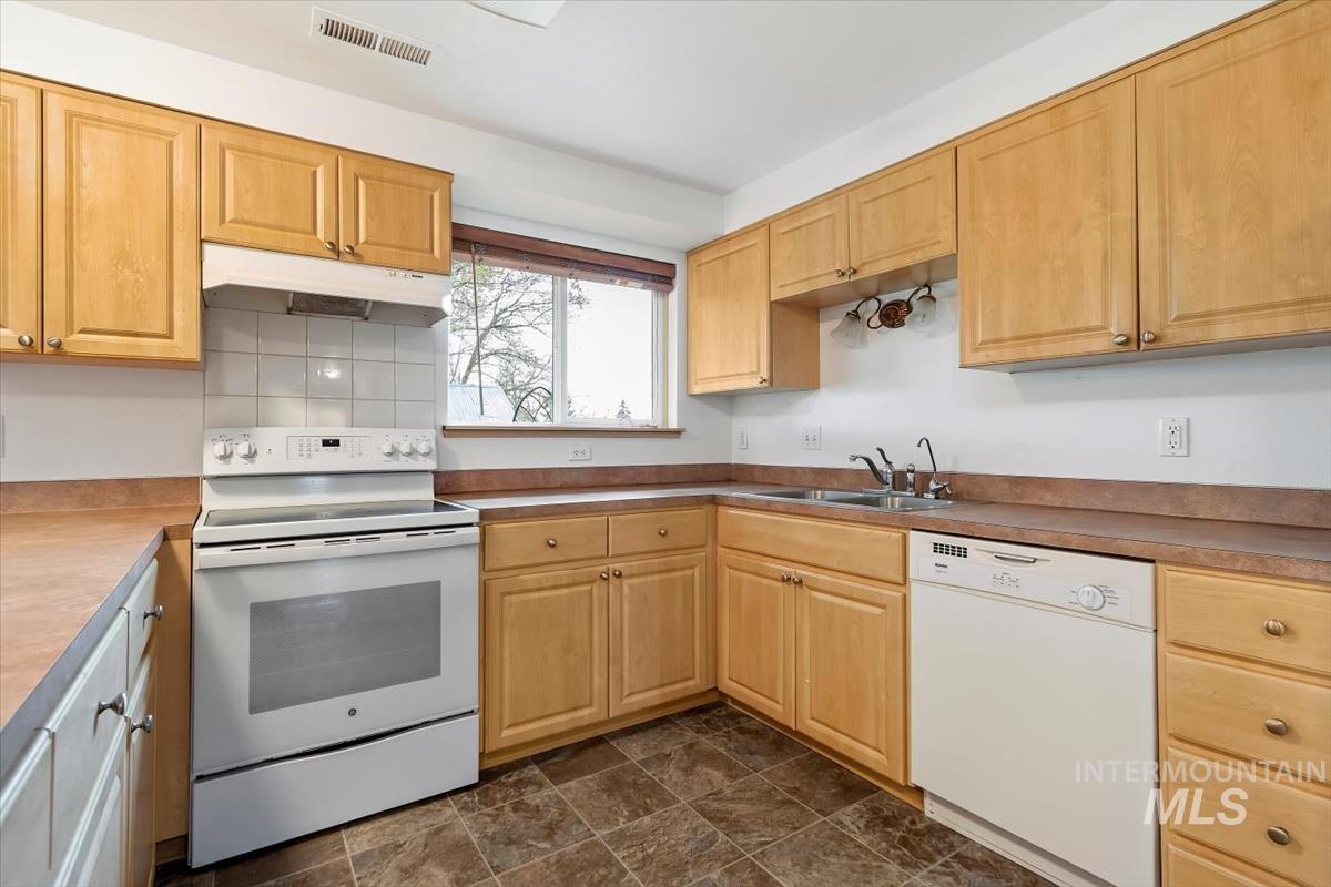 1051 Haas Road Weiser, ID 83672 - Photo 14 of 44 Kitchen featuring white appliances, light wood finish cabinets, light countertops, stone finish floors, and decorative backsplash