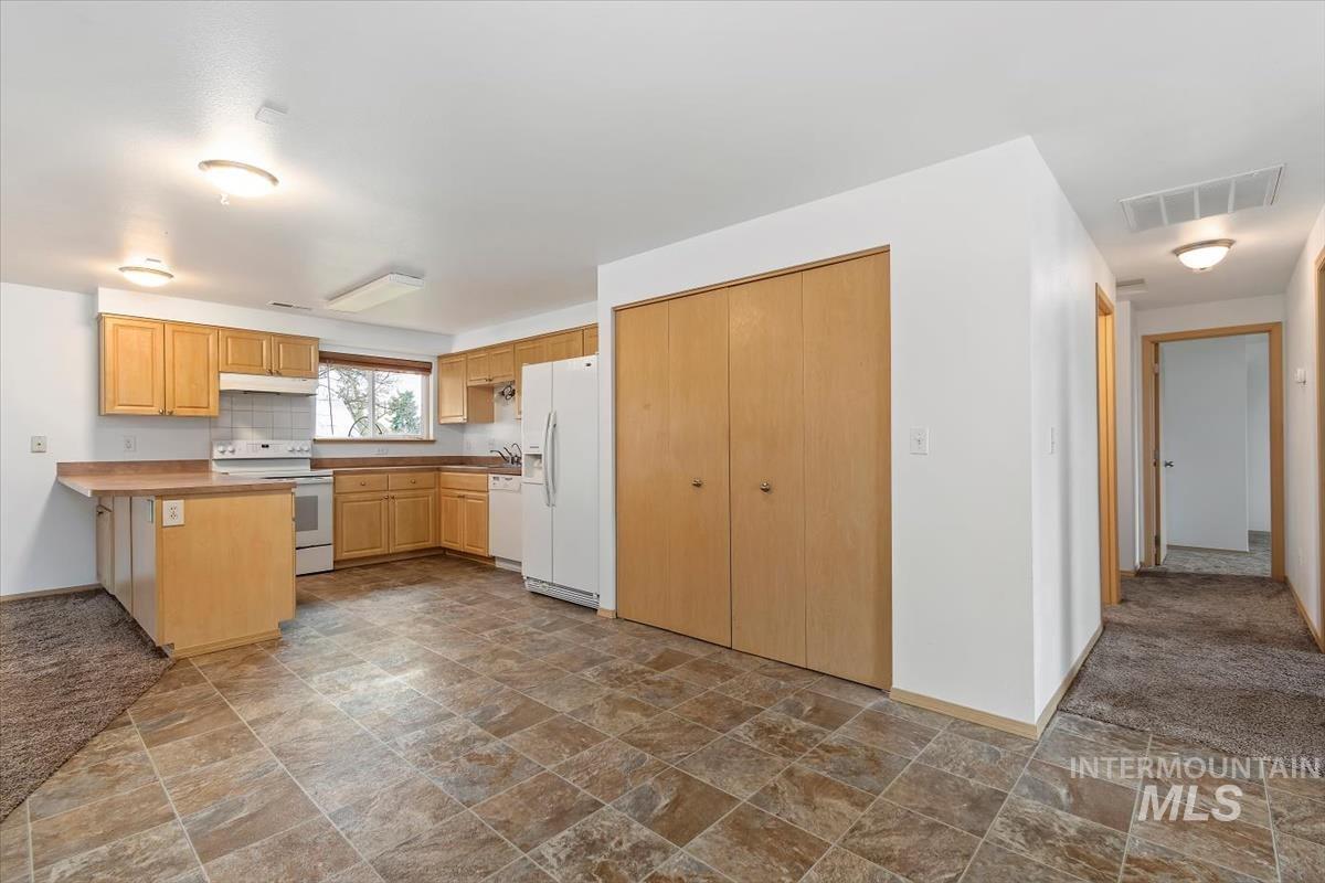1051 Haas Road Weiser, ID 83672 - Photo 19 of 44 Kitchen with stone finish floors, light wood finish cabinets, white appliances, light countertops, and backsplash