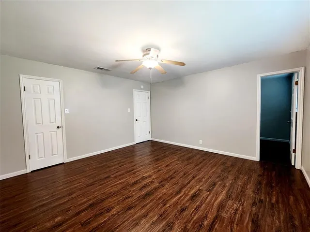 a view of an empty room with wooden floor and a ceiling fan