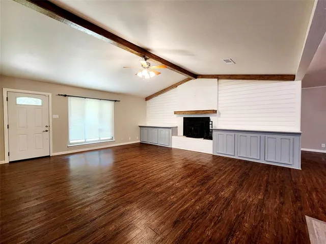 an empty room with wooden floor fireplace and windows