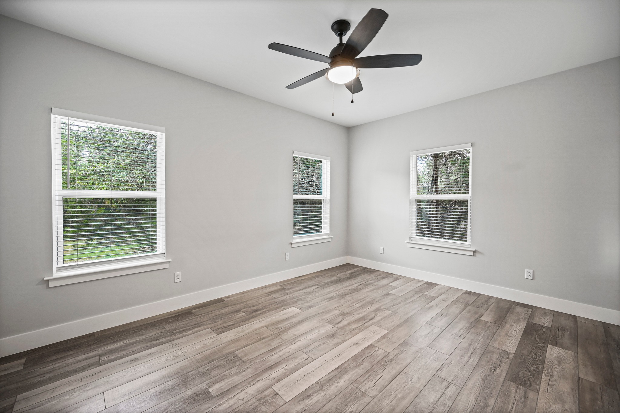 231 North Rainbow Ranch Road Wimberley, TX 78676 - Photo 17 of 40 Four windows illuminate this bedroom, featuring wood-look flooring and a modern ceiling fan.