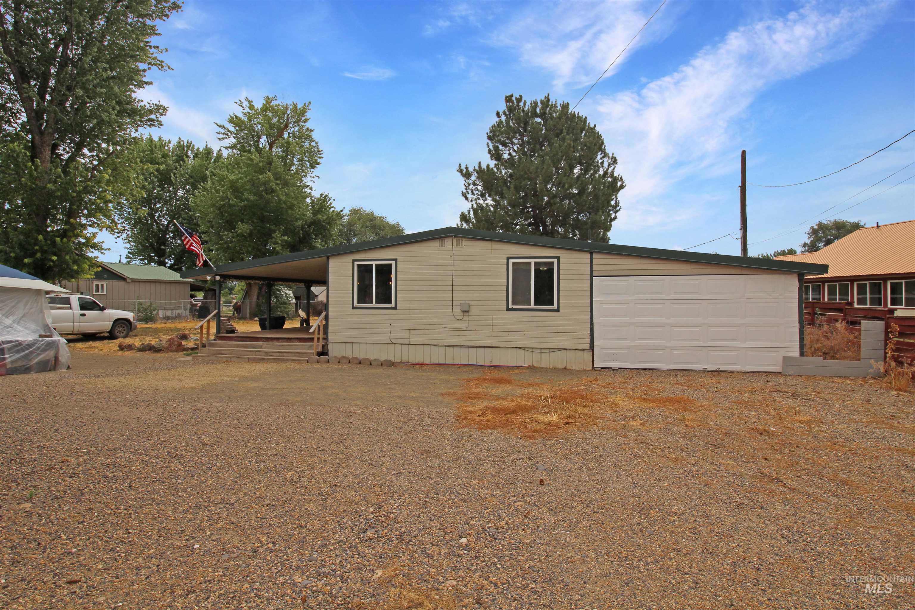 1265 Pioneer Road Weiser, ID 83672 - Photo 26 of 29 Single-story residence featuring light-colored siding, a covered front porch with steps, a white garage door, and a gravel parking area