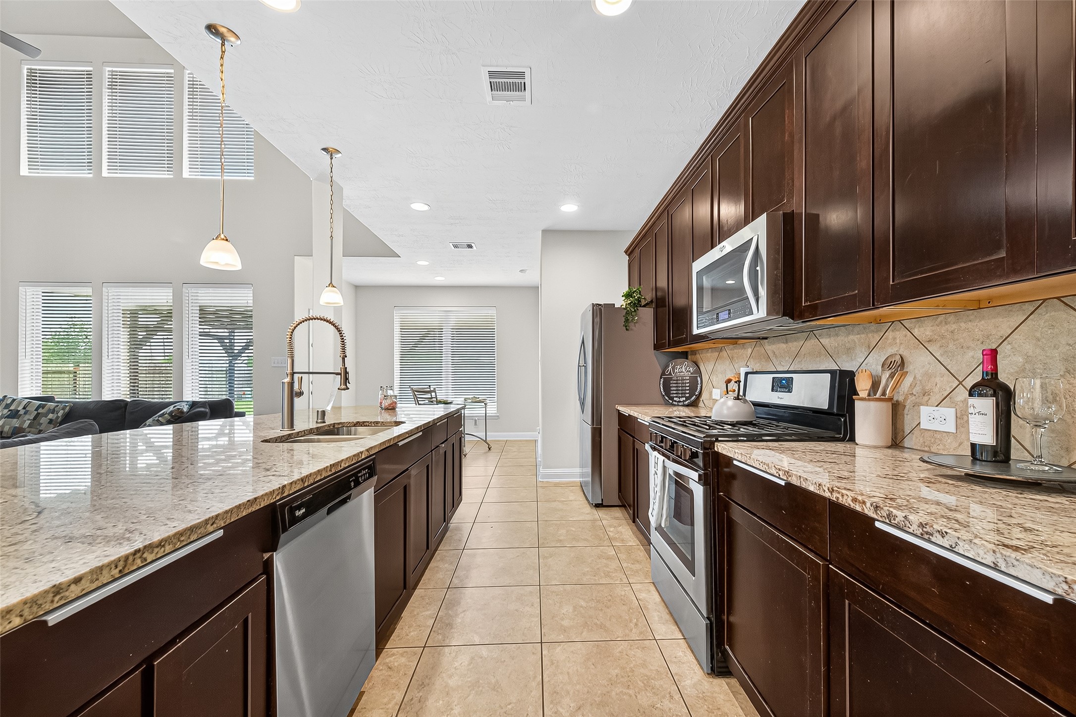 8107 Lockridge Terrace Lane Cypress, TX 77433 - Photo 17 of 50 Another view of the stunning kitchen reveals an expansive layout framed by soaring ceilings and natural light. Granite countertops and rich cabinetry stretch the length of the room, offering generous prep space and storage. This is a chef’s dream with a warm, welcoming heart — the true center of your next chapter.