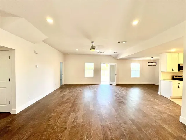 a view of an empty room and a kitchen with wooden floor