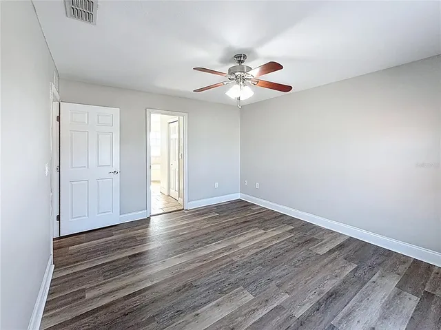 a view of an empty room with wooden floor and a ceiling fan