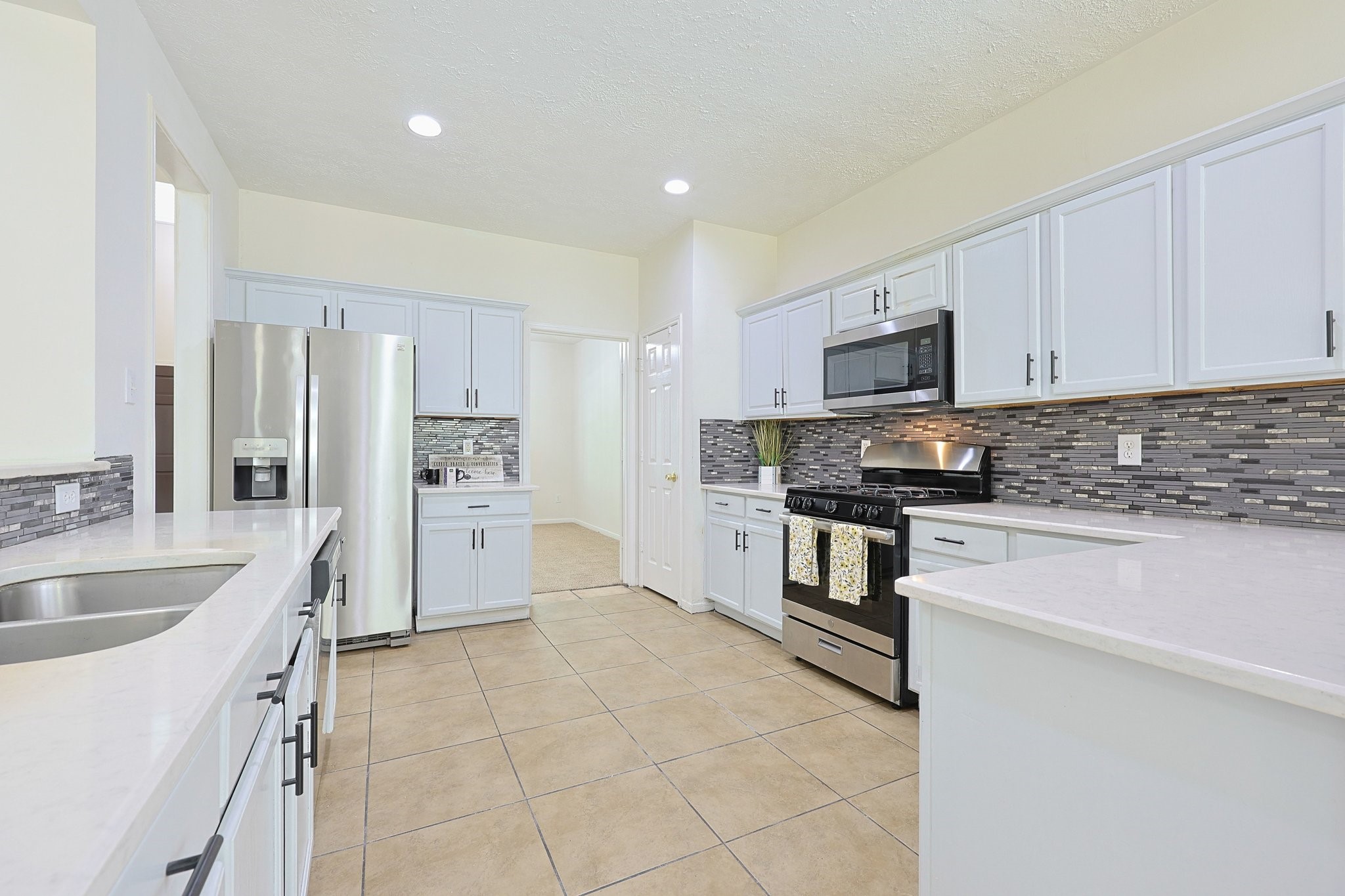 23019 Eastgate Village Drive Spring, TX 77373 - Photo 4 of 46 This kitchen features modern stainless steel appliances, grey cabinetry, and a stylish tile backsplash. It offers ample counter space with a bright, open layout and recessed lighting, making it ideal for cooking and entertaining.
