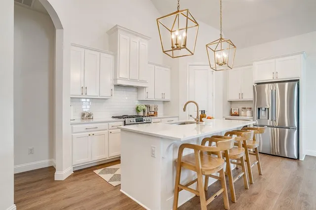 a kitchen with stainless steel appliances granite countertop a sink a stove white cabinets a dining table and chairs