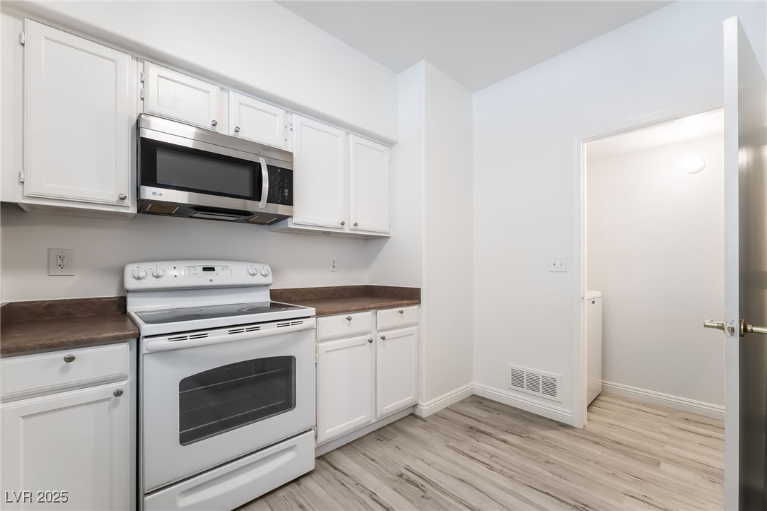 7255 West Sunset Road, Unit 1148 Las Vegas, NV 89113 - Photo 15 of 62 Kitchen with white electric range, dark countertops, stainless steel microwave, light wood finished floors, and white cabinets