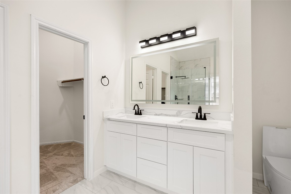 13735 Sablegarden Lane Houston, TX 77014 - Photo 12 of 20 Beautifully updated primary bath featuring a spacious double-sink vanity, modern black fixtures, and a large framed mirror. The walk-in closet and glass-enclosed shower add both convenience and luxury to your daily routine
