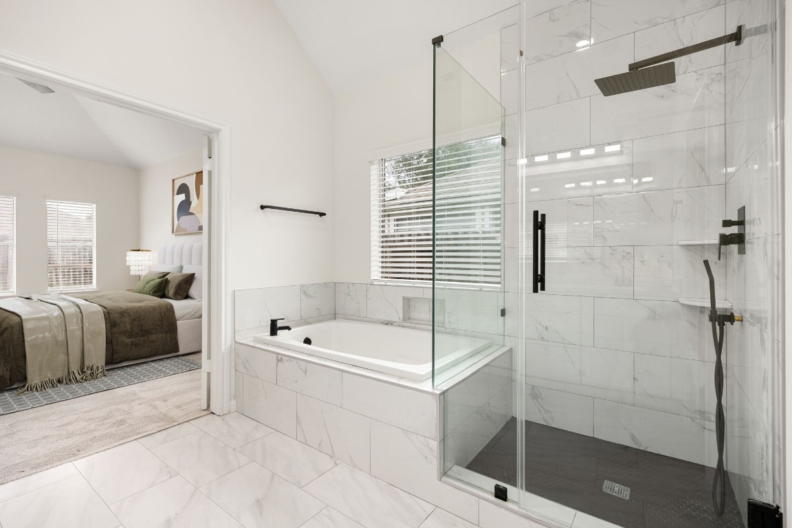13735 Sablegarden Lane Houston, TX 77014 - Photo 13 of 20 Retreat-style primary bath featuring a deep soaking tub, a sleek glass-enclosed shower with modern fixtures, and elegant marble-look tile throughout. The serene connection to the primary bedroom creates a truly relaxing suite