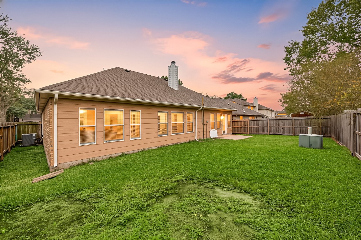 13735 Sablegarden Lane Houston, TX 77014 - Photo 17 of 20 Spacious backyard with endless possibilities—perfect for outdoor dining, play areas, or future landscaping projects. The wide green lawn offers plenty of room to relax or entertain, while the full privacy fence creates a peaceful and secure setting. Large windows along the back of the home invite warm natural light into the interior, creating a seamless indoor–outdoor feel, especially during sunset.