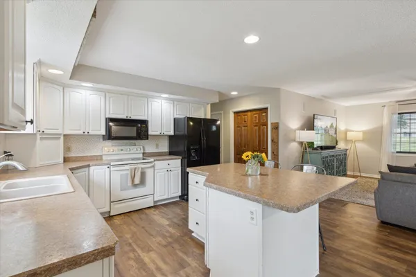 a kitchen with stainless steel appliances a stove top oven a sink a refrigerator white cabinets and wooden floor
