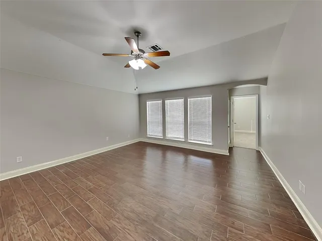 an empty room with wooden floor fan and windows