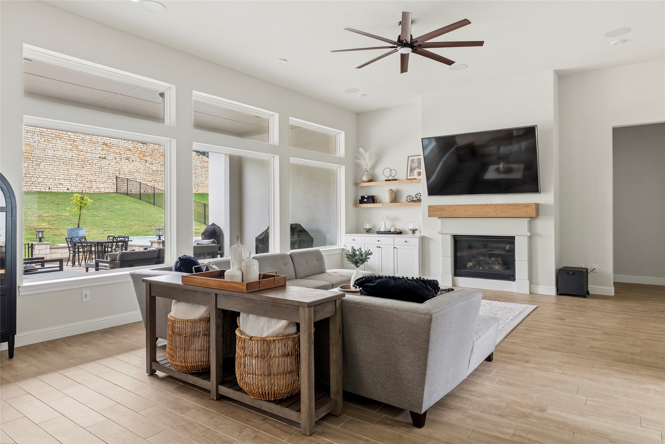 4513 Vieste View Leander, TX 78641 - Photo 15 of 40 Spacious living area featuring large picture windows, a modern ceiling fan, a fireplace with a stone surround and wood mantel, built-in cabinetry, and wood-finish flooring