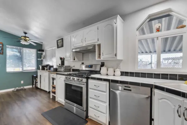 a kitchen with granite countertop a refrigerator a sink dishwasher a stove and white cabinets with wooden floor