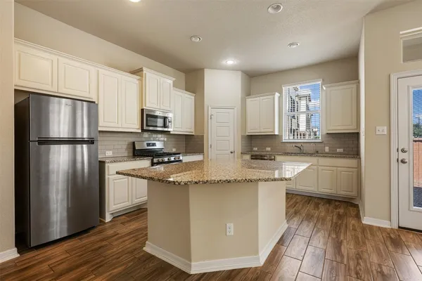 a kitchen with stainless steel appliances granite countertop a refrigerator a stove top oven a sink and dishwasher with wooden floor