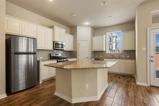 a kitchen with stainless steel appliances granite countertop a refrigerator a stove top oven a sink and dishwasher with wooden floor