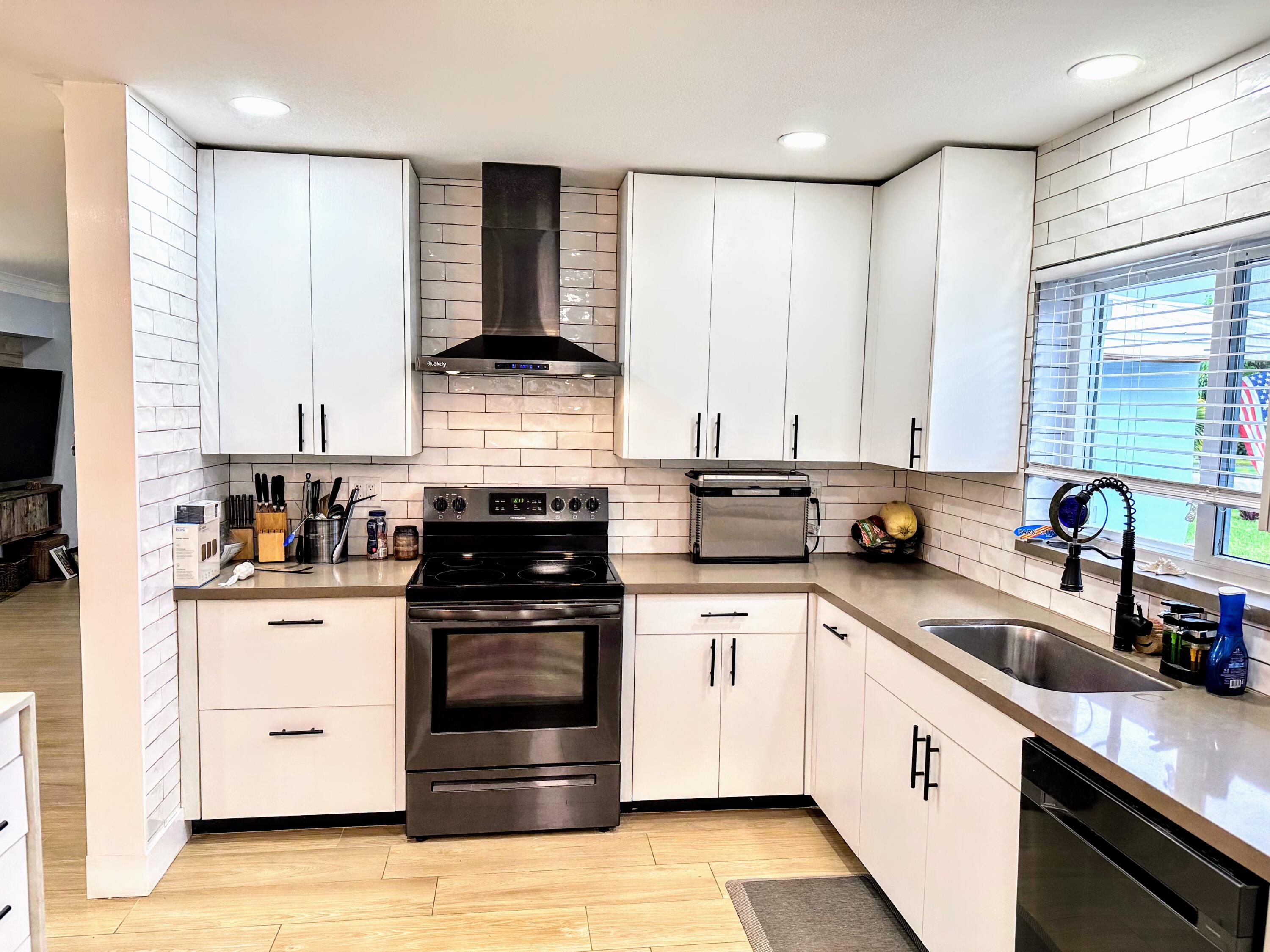 469 Northeast 30th Street Boca Raton, FL 33431 - Photo 7 of 24 a kitchen with stainless steel appliances granite countertop white cabinets a sink a stove a refrigerator and island with wooden floor