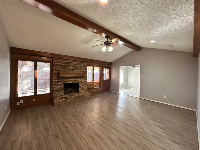 an empty room with wooden floor fireplace and windows