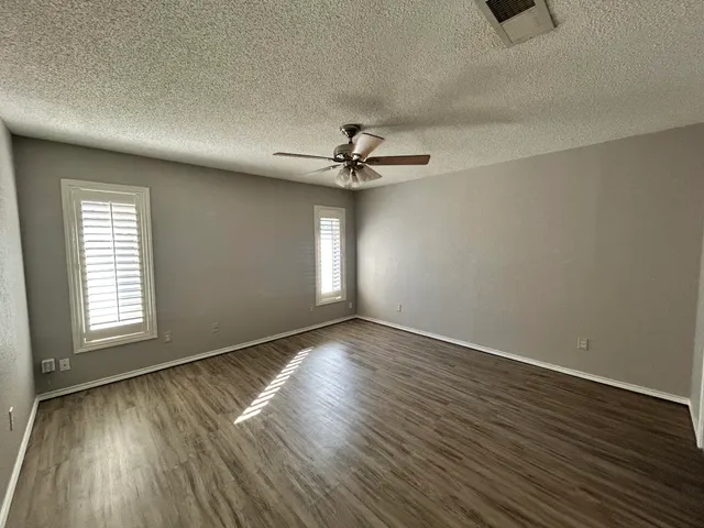 an empty room with wooden floor chandelier fan and windows
