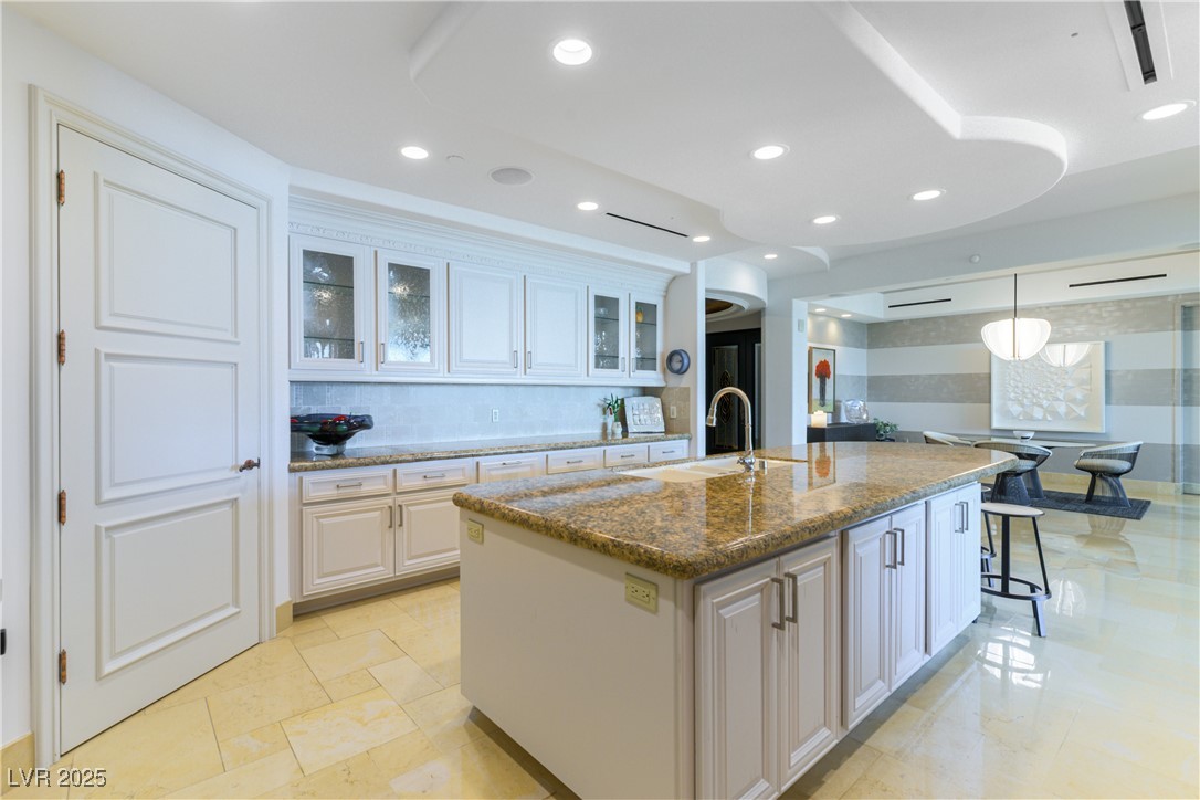 9101 Alta Drive, Unit 505 Las Vegas, NV 89145 - Photo 6 of 64 Kitchen featuring tasteful backsplash, glass insert cabinets, an island with sink, dark stone countertops, and recessed lighting