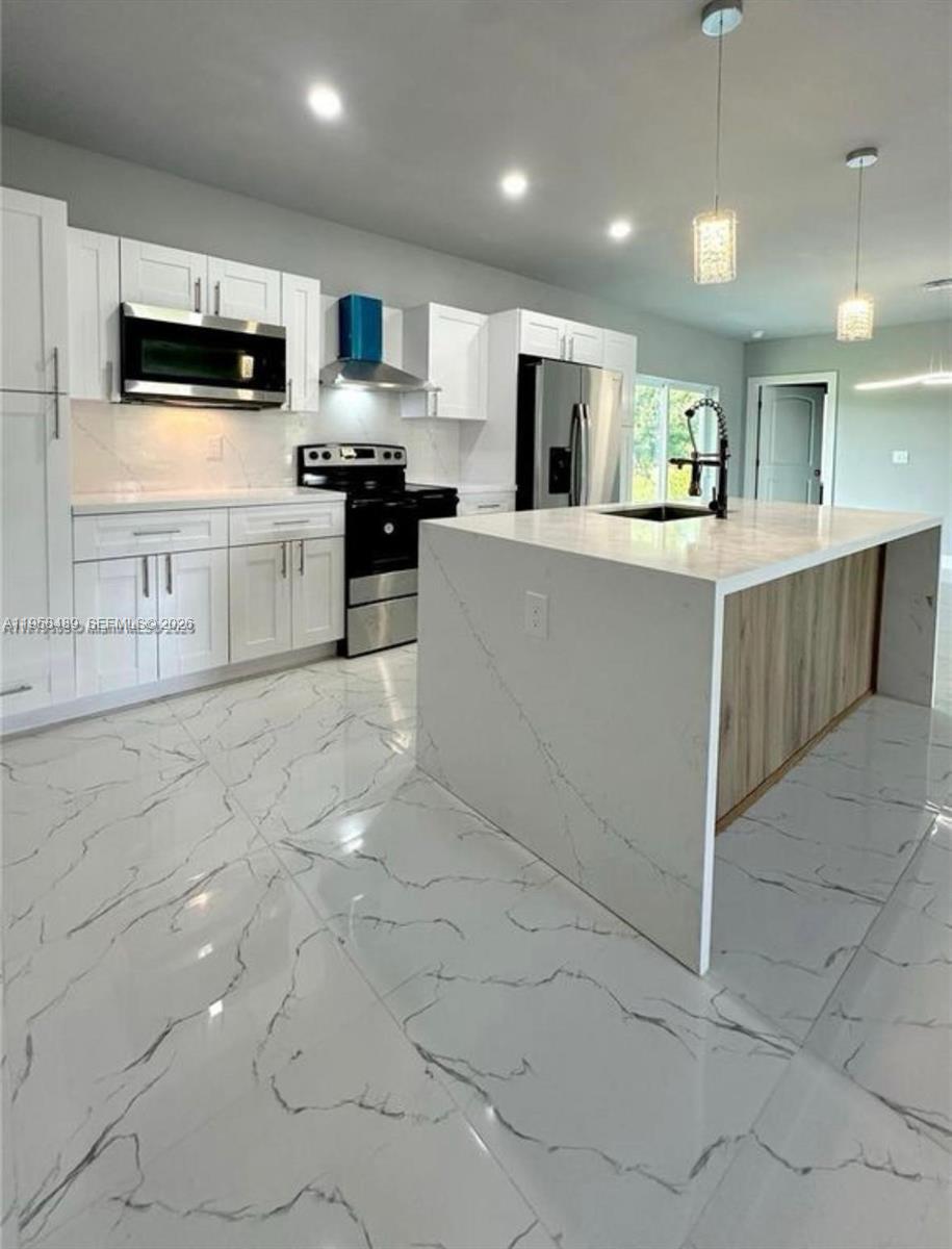 868 Cervantes Street East Lehigh Acres, FL 33974 - Photo 5 of 18 a large white kitchen with kitchen island granite countertop a stove top oven a sink a counter top space and cabinets