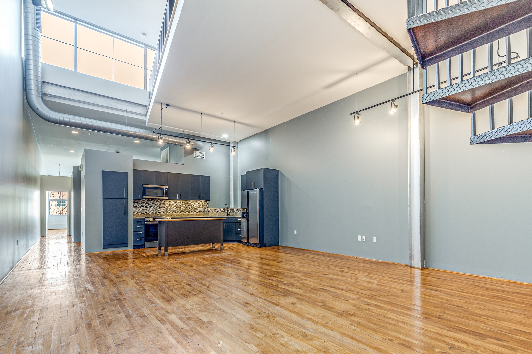 1312 Live Oak Street, Unit 223 Houston, TX 77003 - Photo 1 of 31 Primary living area featuring soaring ceilings, exposed ductwork, and expansive hardwood floors, creating a bright and open industrial style space ideal for modern living.