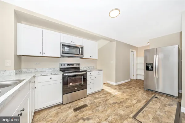 a kitchen with granite countertop a refrigerator stove and white cabinets
