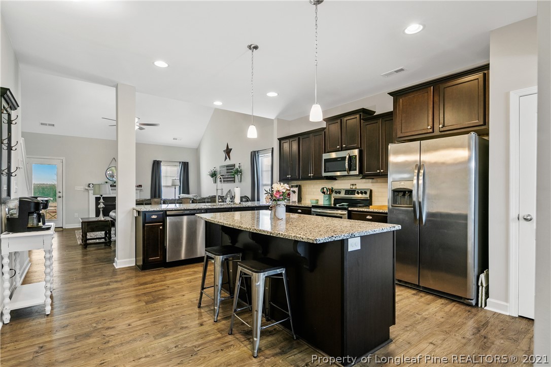 244 Mill Ridge Court Godwin, NC 28344 - Photo 10 of 50 a kitchen with stainless steel appliances kitchen island granite countertop a refrigerator a stove a sink a dining table and chairs with wooden floor