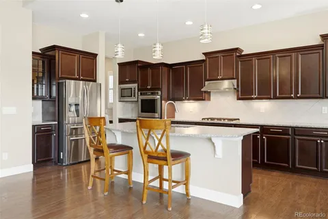a kitchen with stainless steel appliances kitchen island granite countertop a refrigerator a stove top oven and a sink with wooden floor